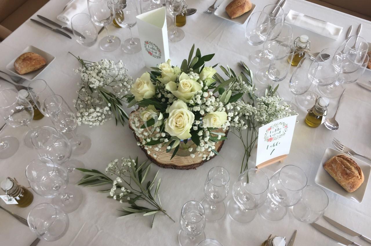 Table dressée avec une décoration florale centrale composée de roses blanches et gypsophiles, entourée de couverts et pains.