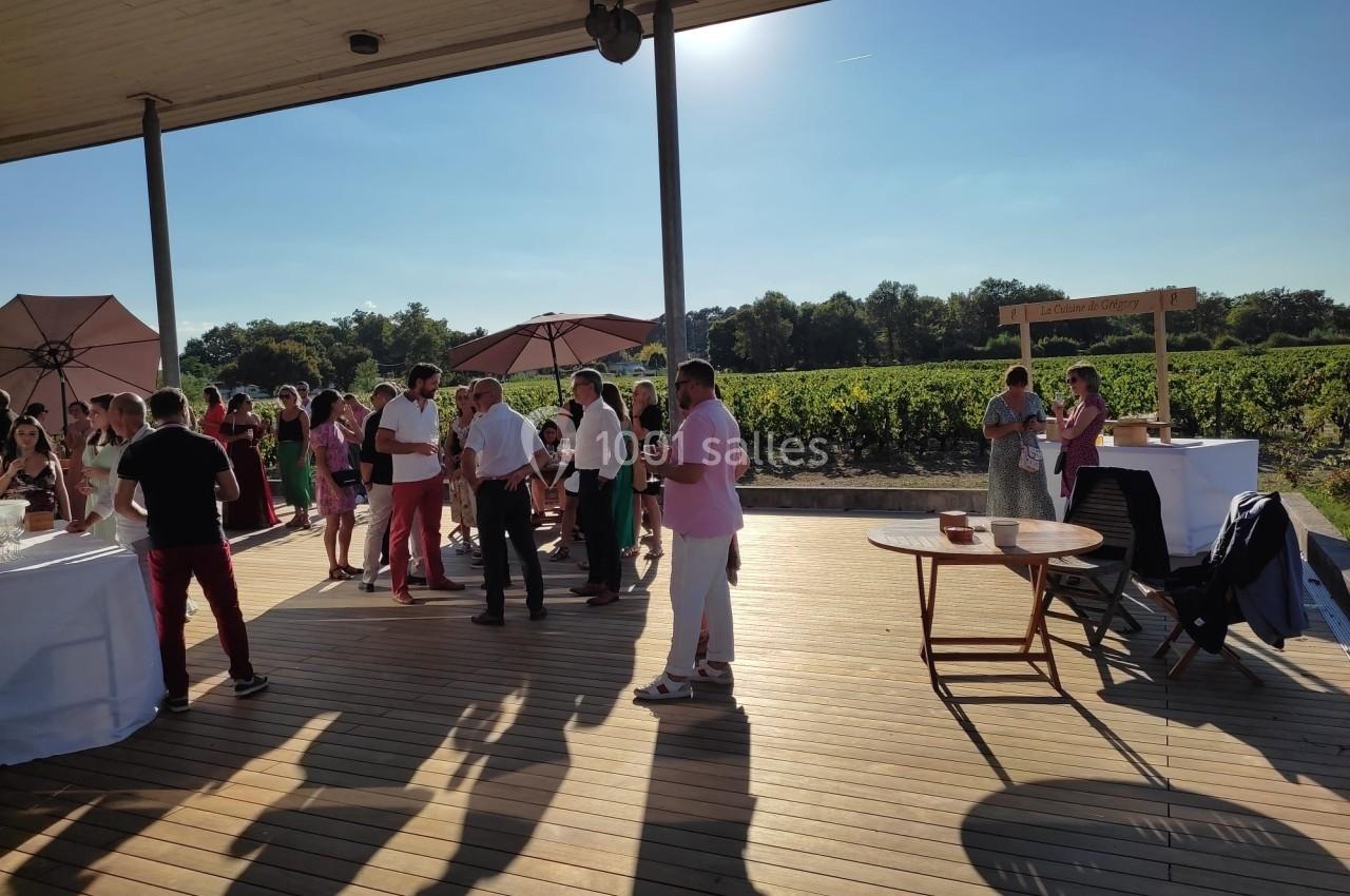 Personnes rassemblées sur une terrasse en bois, près de vignobles, sous un ciel dégagé en fin de journée.