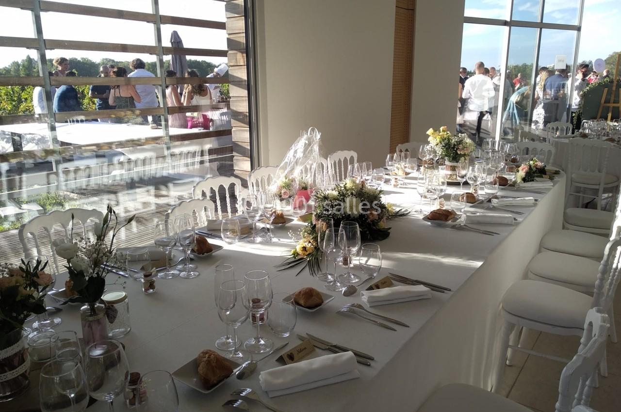 Table élégamment dressée pour un événement, avec nappes blanches, verres, couverts et compositions florales.