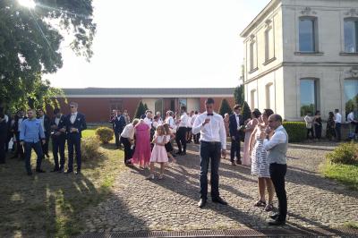 Un groupe de personnes échange autour d'un buffet en plein air, avec des serveurs et un paysage de vignoble en arrière-plan.