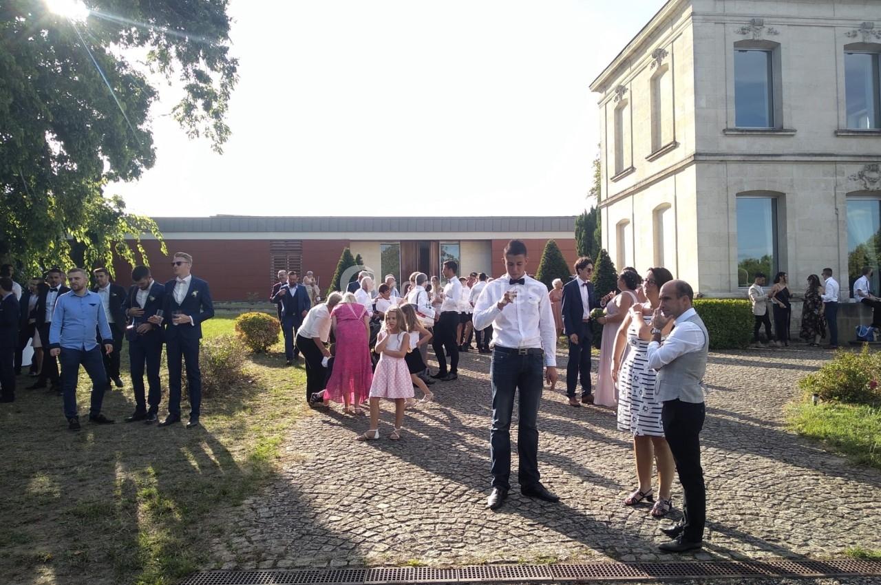Groupe de personnes rassemblées en extérieur devant un bâtiment, certaines discutant ou prenant des photos.