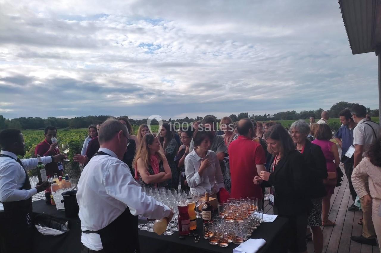 Un groupe de personnes échange autour d'un buffet en plein air, avec des serveurs et un paysage de vignoble en arrière-plan.