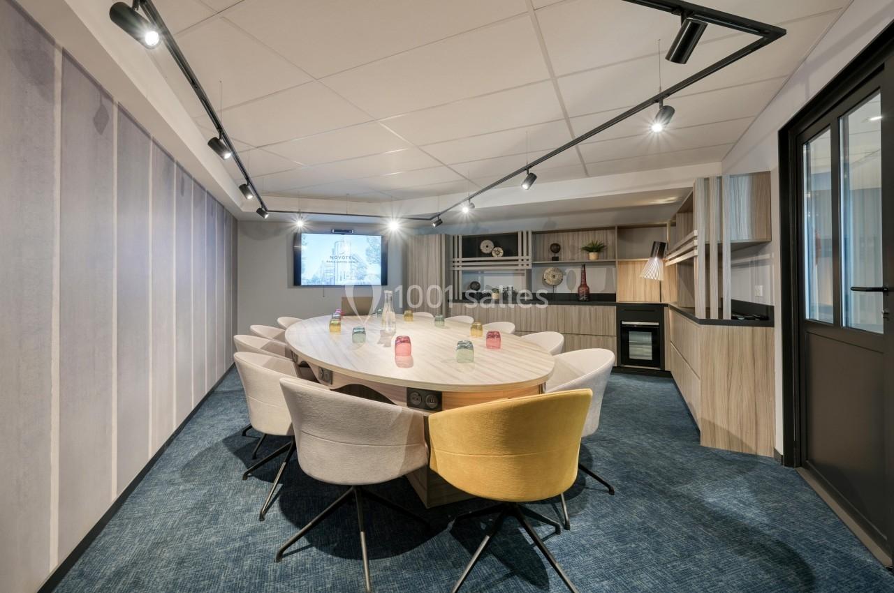 Salle de réunion moderne avec table ovale, chaises colorées, éclairage suspendu et étagères décoratives en arrière-plan.