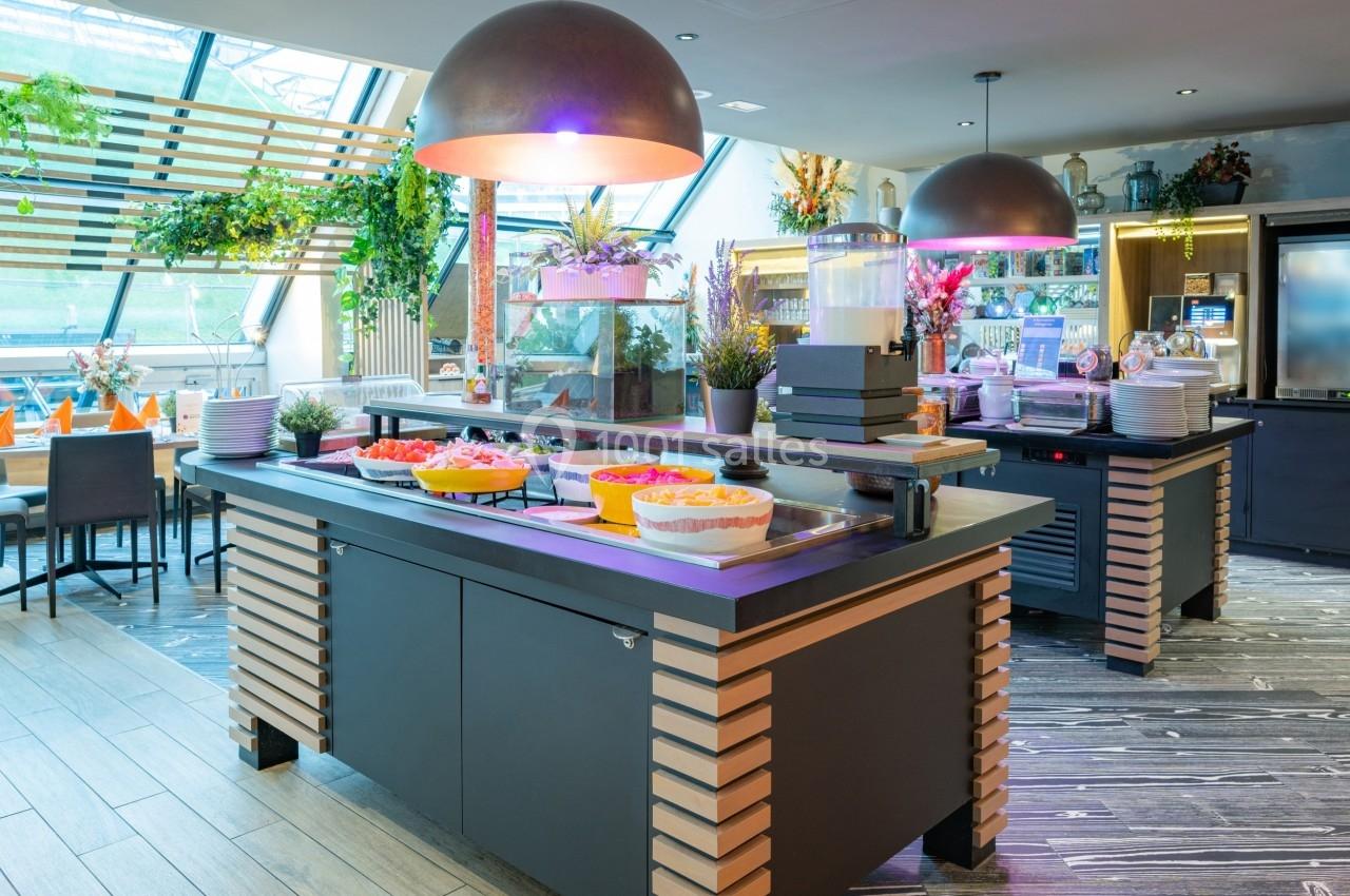 Buffet de restaurant avec plats variés, boissons et décoration végétale dans un espace lumineux et moderne.