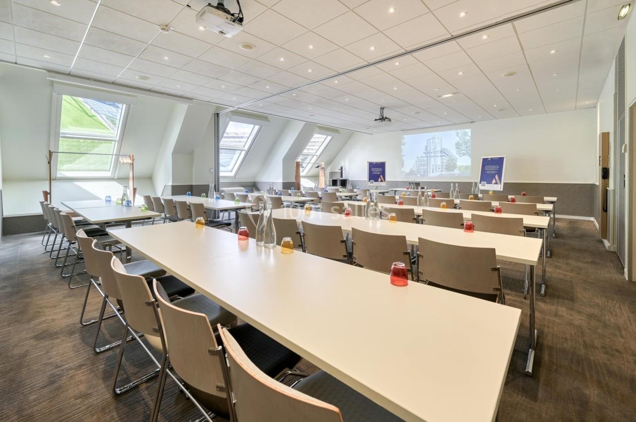 Salle de réunion lumineuse avec des tables alignées, des chaises et un projecteur installé au plafond.