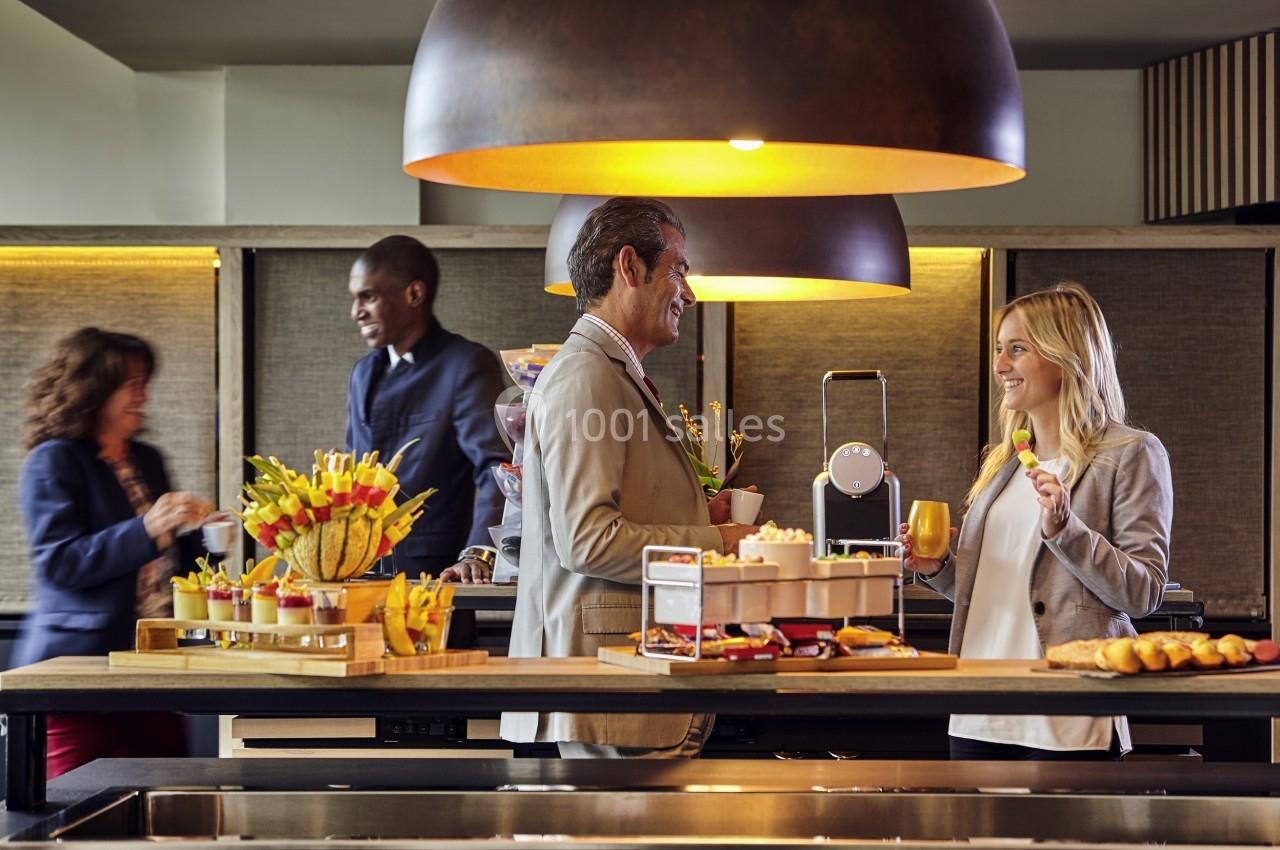 Des personnes discutent et se servent autour d'un buffet avec des boissons et des collations dans un cadre convivial.