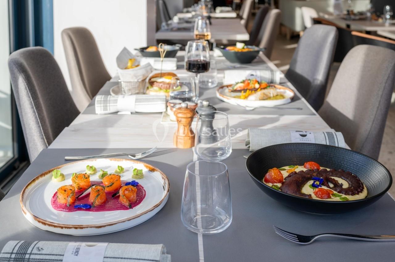 Tables dressées avec des plats raffinés, comprenant des assiettes colorées et des verres dans un restaurant lumineux.