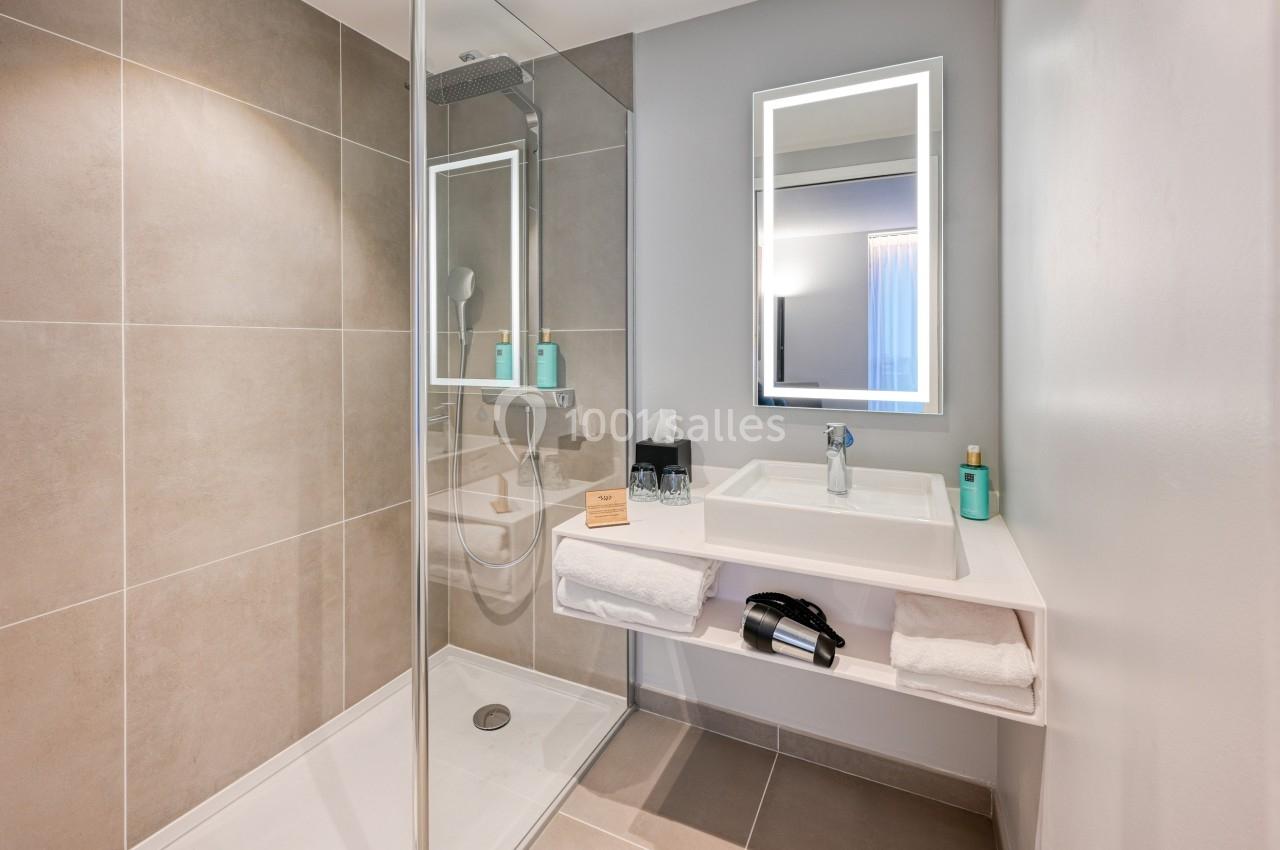 Salle de bain moderne avec douche à l'italienne, lavabo avec miroir éclairé et accessoires de toilette.