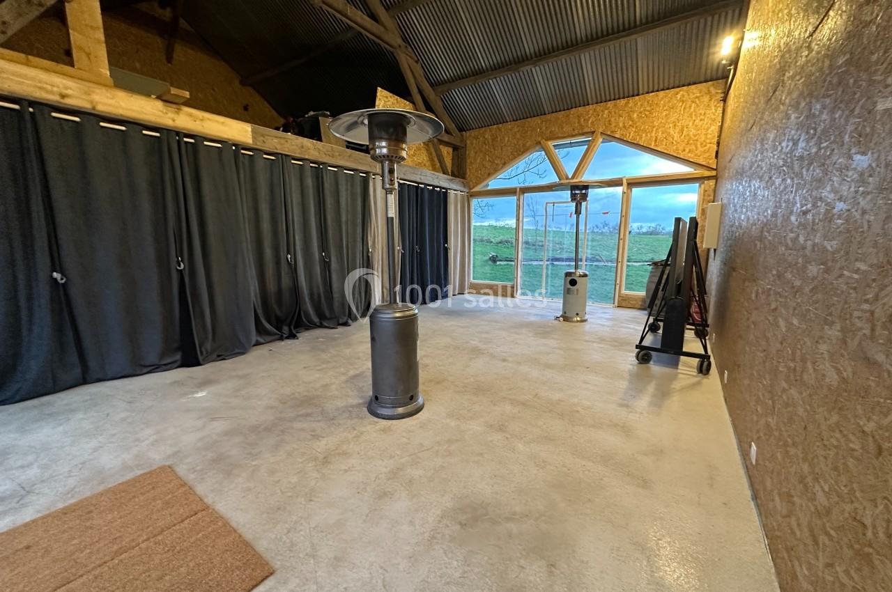 Intérieur d'une salle avec sol en béton, murs en bois, rideaux noirs, chauffages et grande baie vitrée donnant sur un…