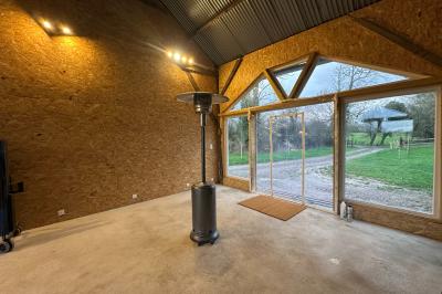 Intérieur d'une pièce avec grandes baies vitrées, murs en bois, un chauffage mobile et un conteneur bleu.