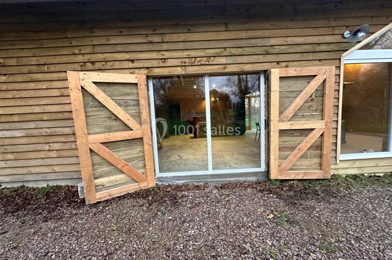 Façade en bois avec une porte vitrée coulissante encadrée de volets ouverts, donnant sur un intérieur éclairé.