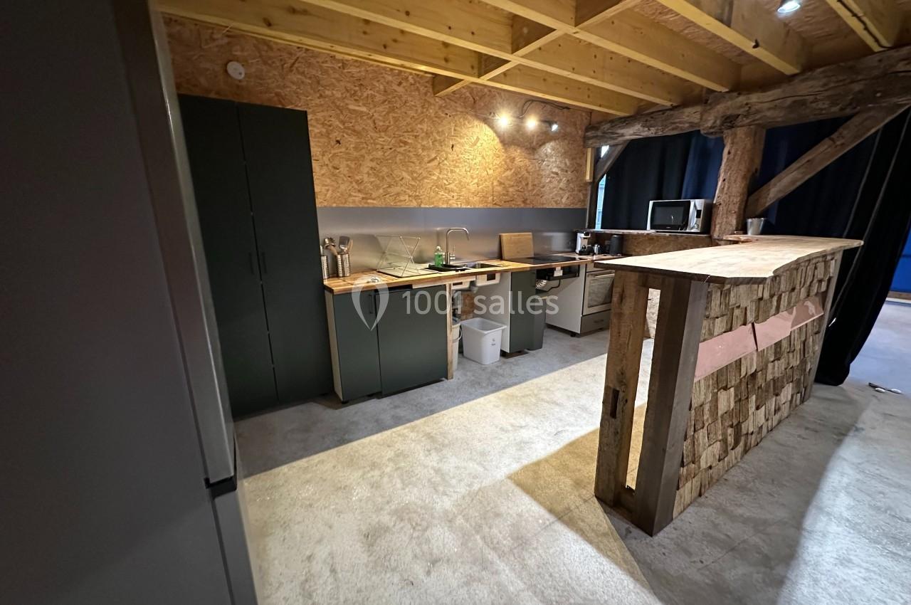 Cuisine rustique avec plan de travail en bois, armoires vertes, poutres apparentes et éclairage chaleureux.