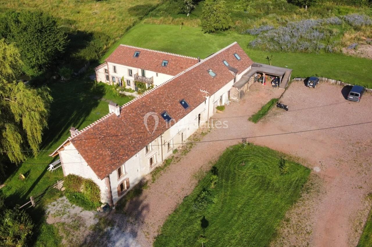 Vue aérienne d'une grande maison en pierre avec toit en tuiles, entourée de pelouses et d'un parking en gravier.
