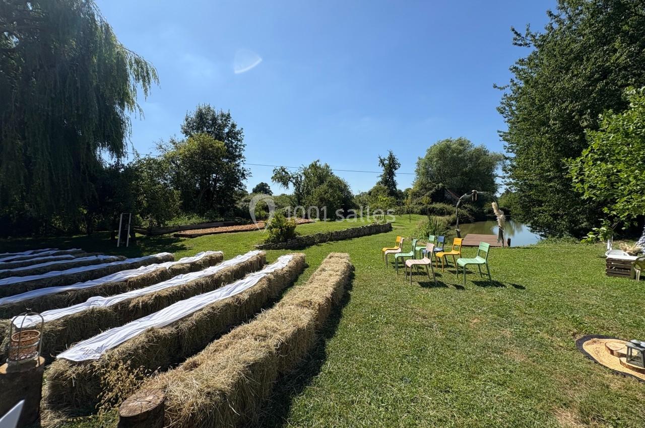 Bottes de paille disposées en rangées pour une cérémonie en plein air, avec des chaises colorées et un étang en arrière-plan.