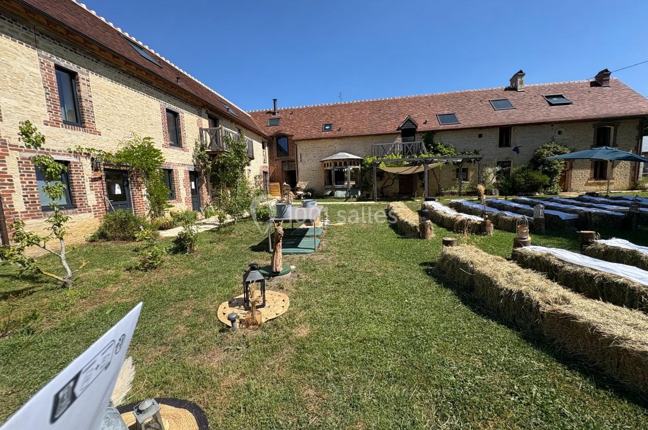 Cour intérieure d'une ferme rénovée avec des bâtiments en pierre, des bottes de paille et des tables installées pour un…