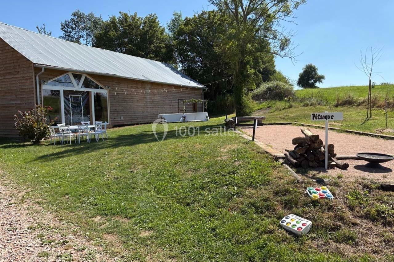 Terrain de pétanque en plein air près d'un bâtiment en bois, entouré de verdure et d'arbres.
