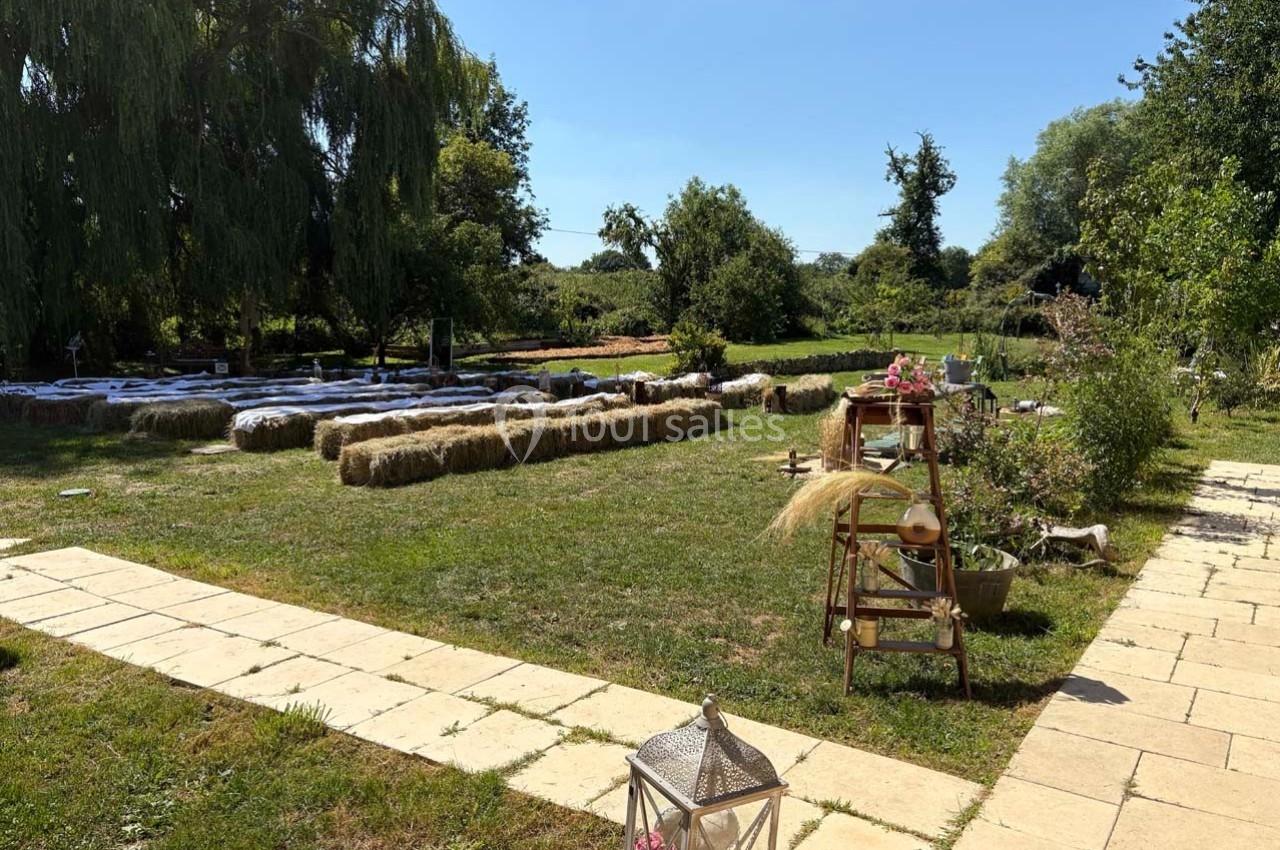 Allée pavée menant à un espace extérieur aménagé avec bottes de foin, chaises et décorations florales sous un ciel dégagé.