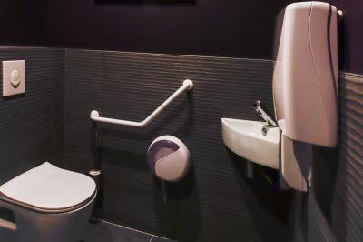Toilettes accessibles avec barre d'appui, lavabo mural et distributeur de savon dans un espace sombre.