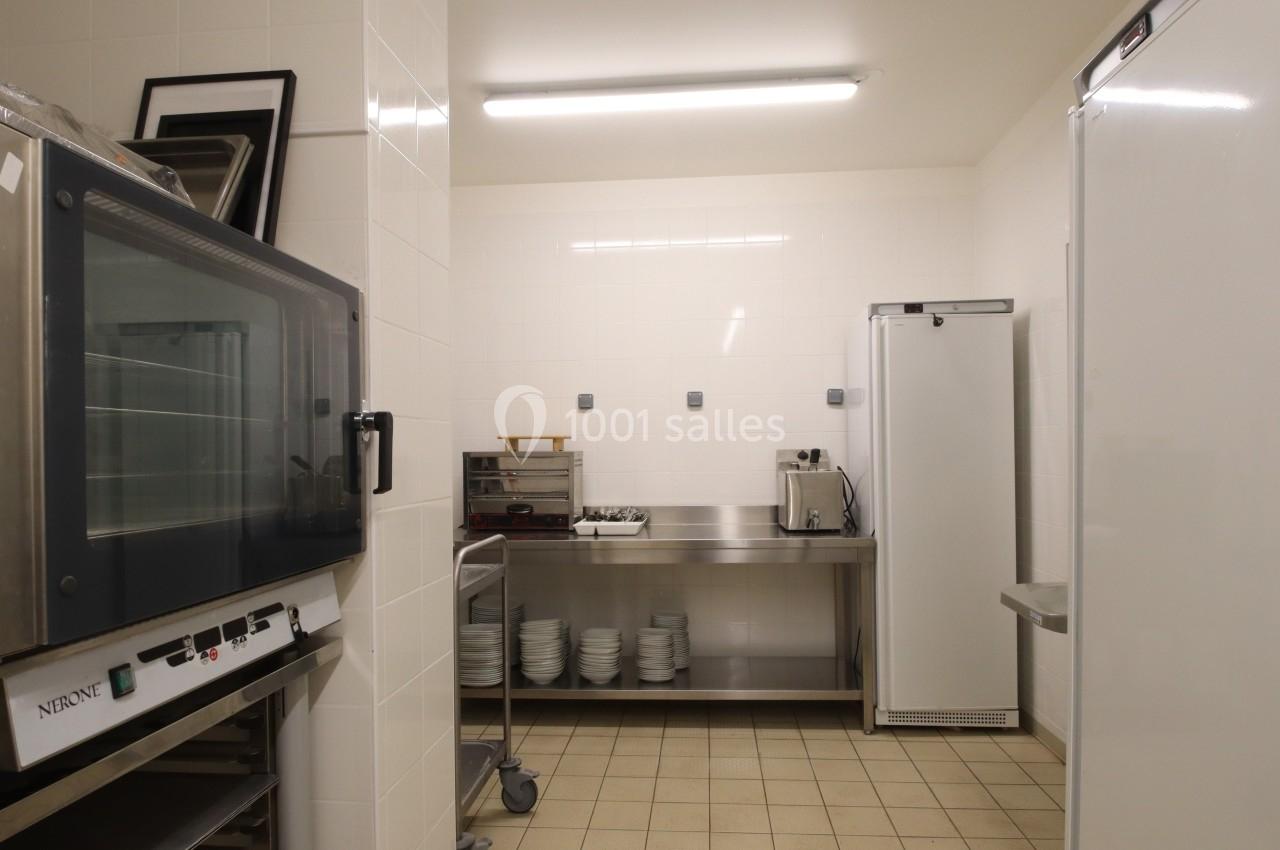 Cuisine professionnelle équipée avec four, réfrigérateur, étagères en inox et vaisselle rangée sur des étagères.