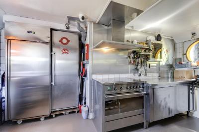 Cuisine professionnelle avec réfrigérateur en inox, four, hotte, étagères murales et plan de travail en acier inoxydable.