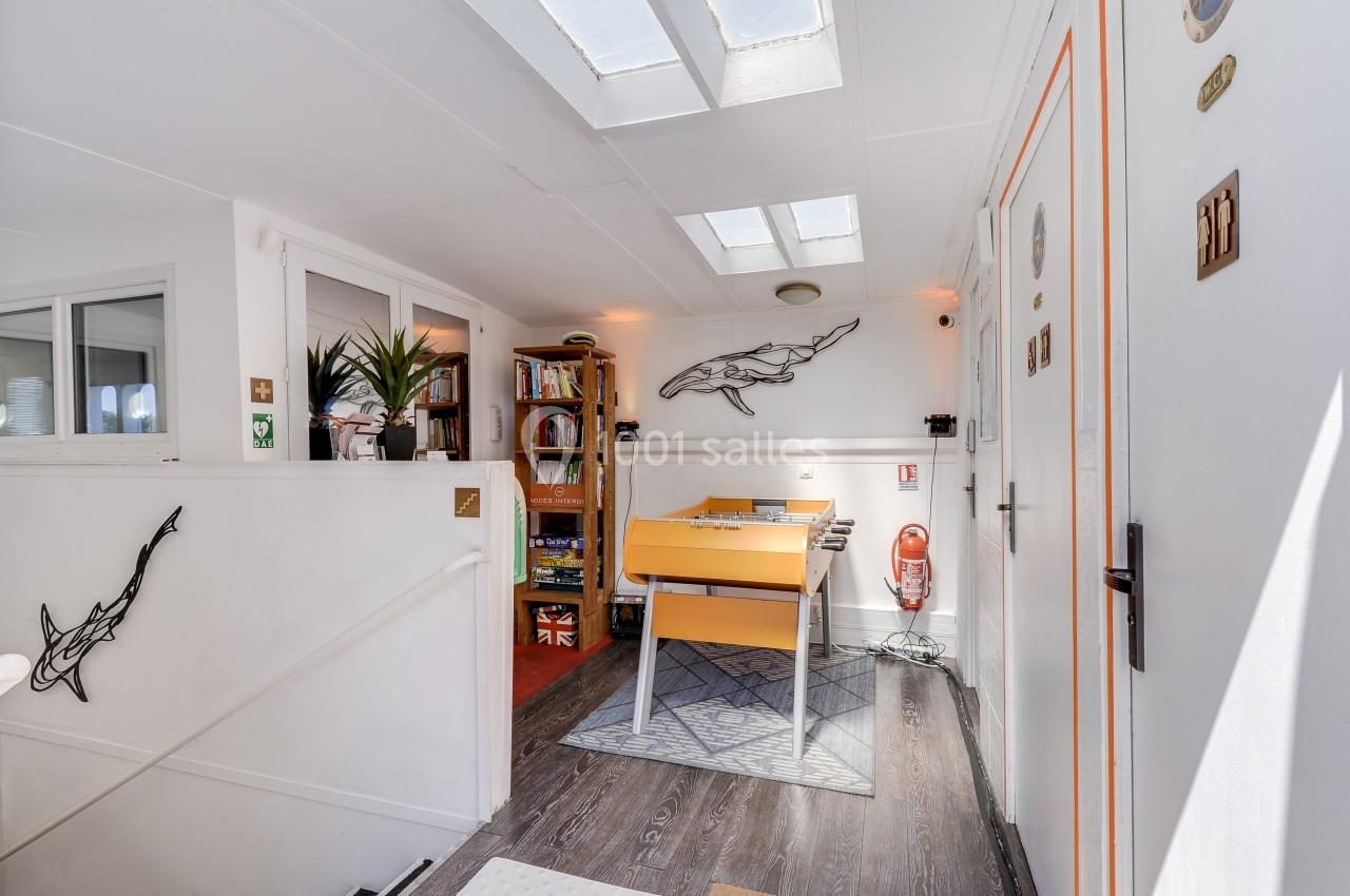 Espace lumineux avec un baby-foot orange, des étagères de livres, des décorations murales et des puits de lumière.