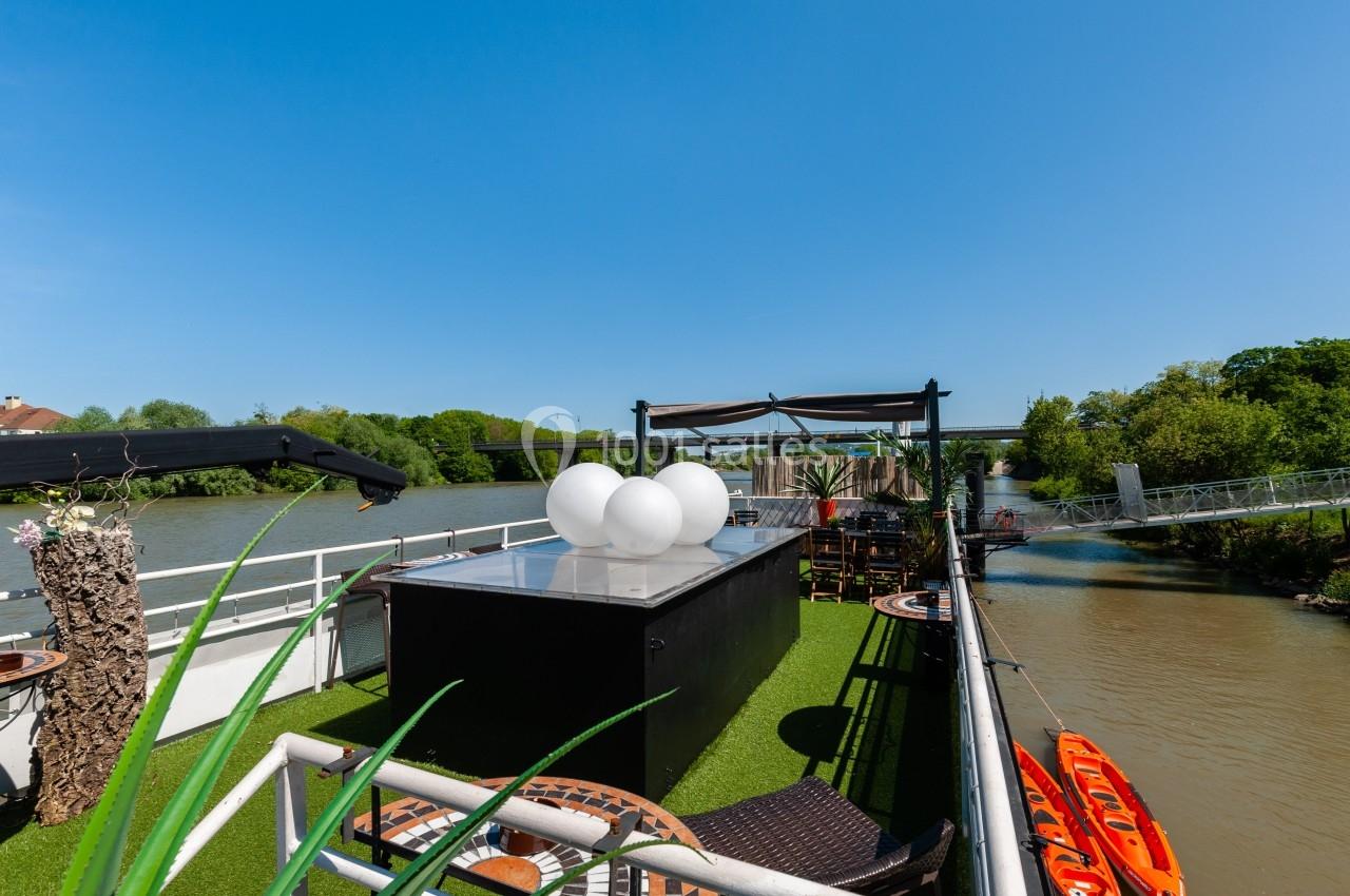 Terrasse aménagée sur une péniche avec gazon artificiel, mobilier d'extérieur et vue sur un cours d'eau bordé de verdure.