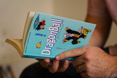 Une personne lit un manga ’Dragon Ball’ avec une couverture bleue illustrée de personnages.