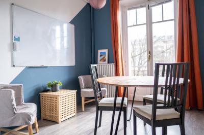 Salle lumineuse avec table ronde, chaises, tableau blanc, fauteuils et fenêtre donnant sur un extérieur arboré.