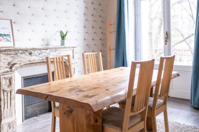 Salle lumineuse avec table ronde, chaises, tableau blanc, fauteuils et fenêtre donnant sur un extérieur arboré.