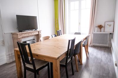 Salle lumineuse avec table ronde, chaises, tableau blanc, fauteuils et fenêtre donnant sur un extérieur arboré.