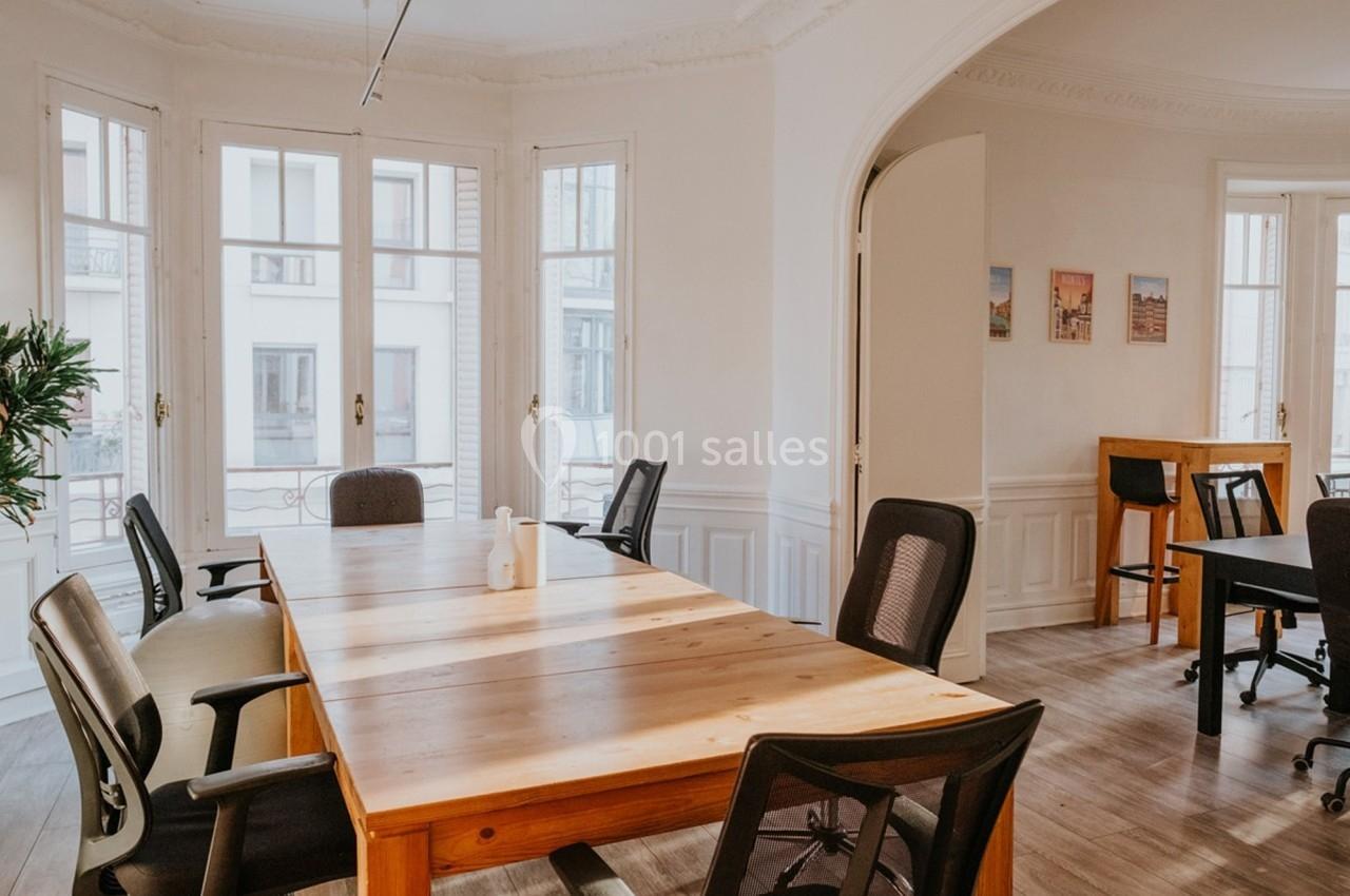 Salle de réunion lumineuse avec une grande table en bois, des chaises noires et des fenêtres donnant sur l'extérieur.
