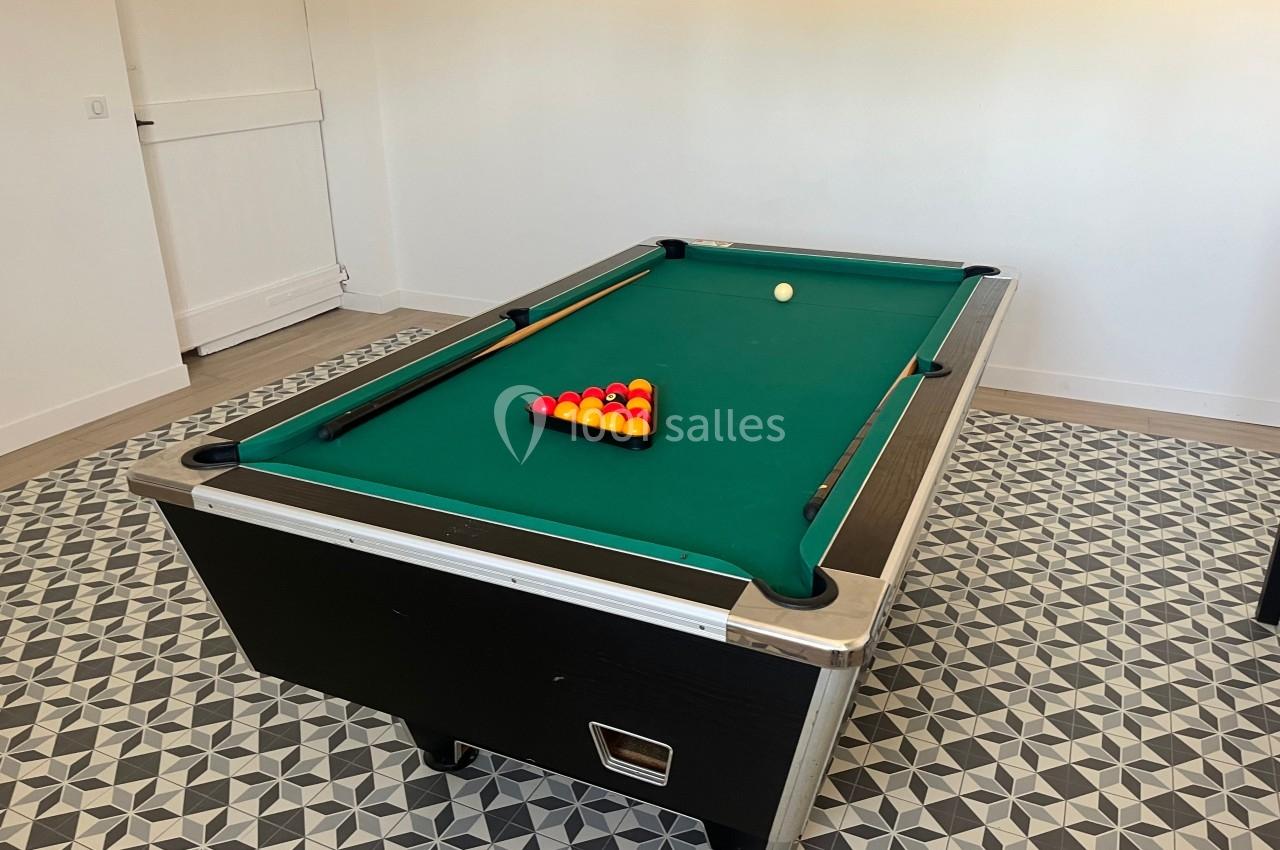 Table de billard avec tapis vert, triangle de boules rouges et jaunes alignées, dans une pièce au sol carrelé.
