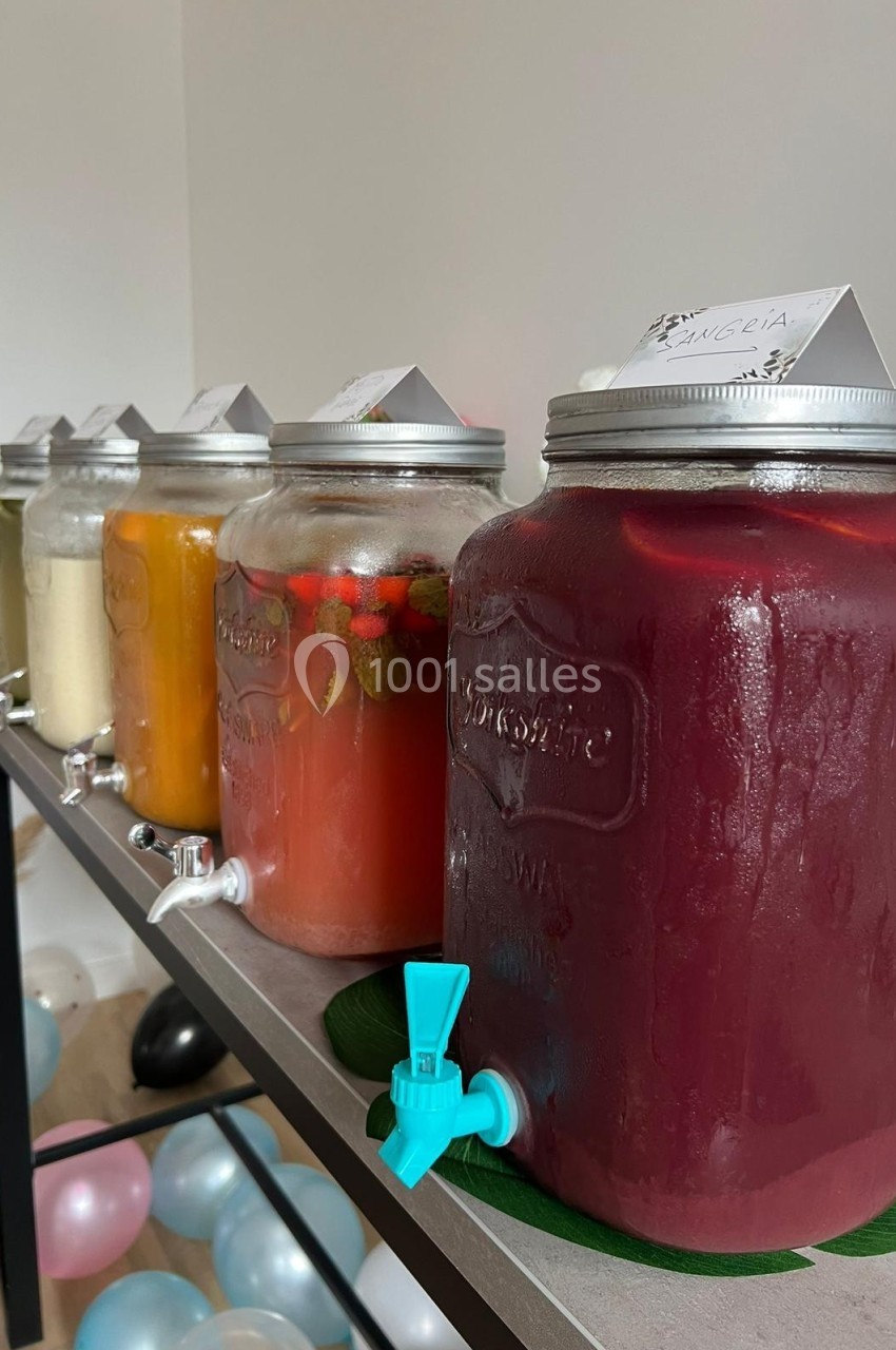 Bocaux en verre alignés sur une table, contenant différentes boissons colorées avec robinets pour le service.