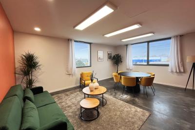 Salle de réception lumineuse avec tables rondes dressées, décorées de fleurs blanches et verdure.