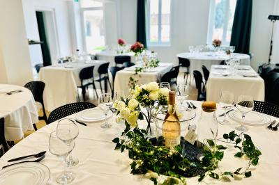 Salle de réception lumineuse avec tables rondes dressées, décorées de fleurs blanches et verdure.