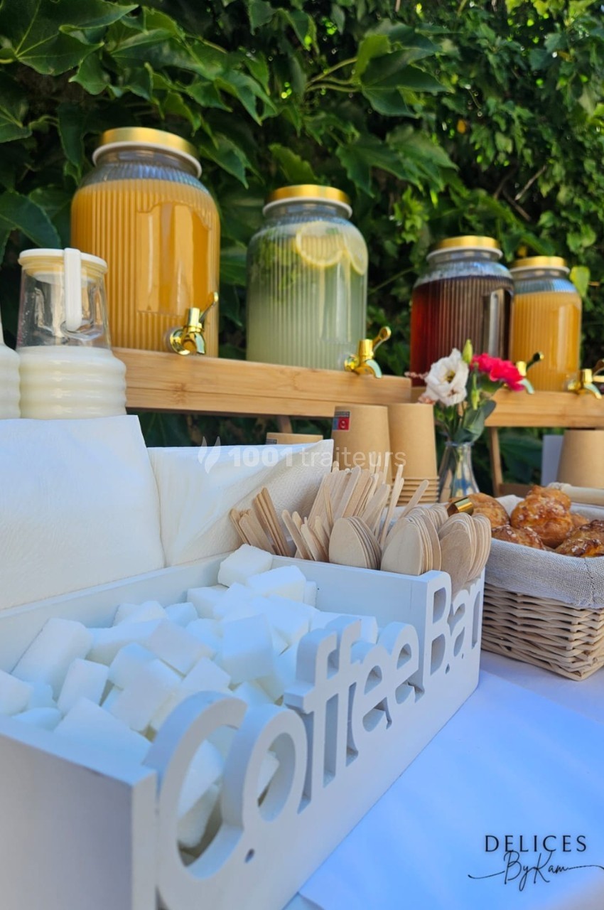 Buffet en plein air avec boissons en distributeurs, lait, sucre en morceaux, couverts en bois et viennoiseries.