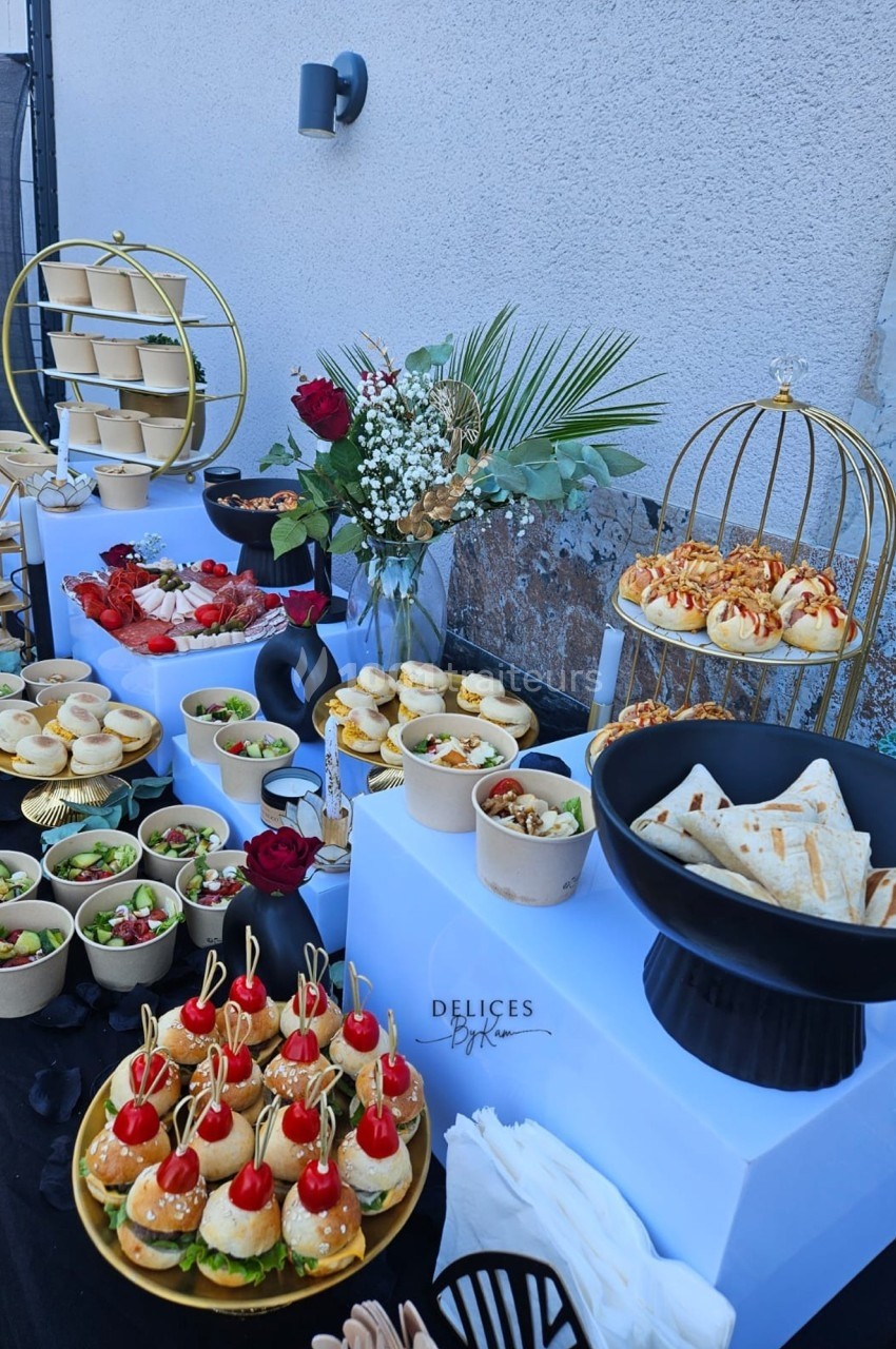 Buffet extérieur avec mini-sandwichs, salades, wraps et desserts, décoré de fleurs et éléments dorés.