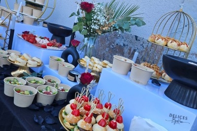 Buffet décoré avec des fleurs, fruits frais, verrines, mini-burgers et desserts, présenté sur une table élégante.