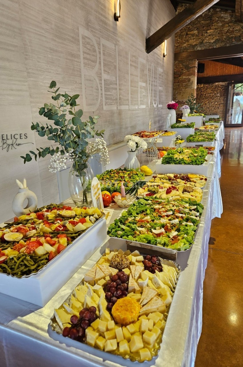 Buffet varié avec salades, fromages, fruits et décorations florales, présenté sur une longue table blanche.