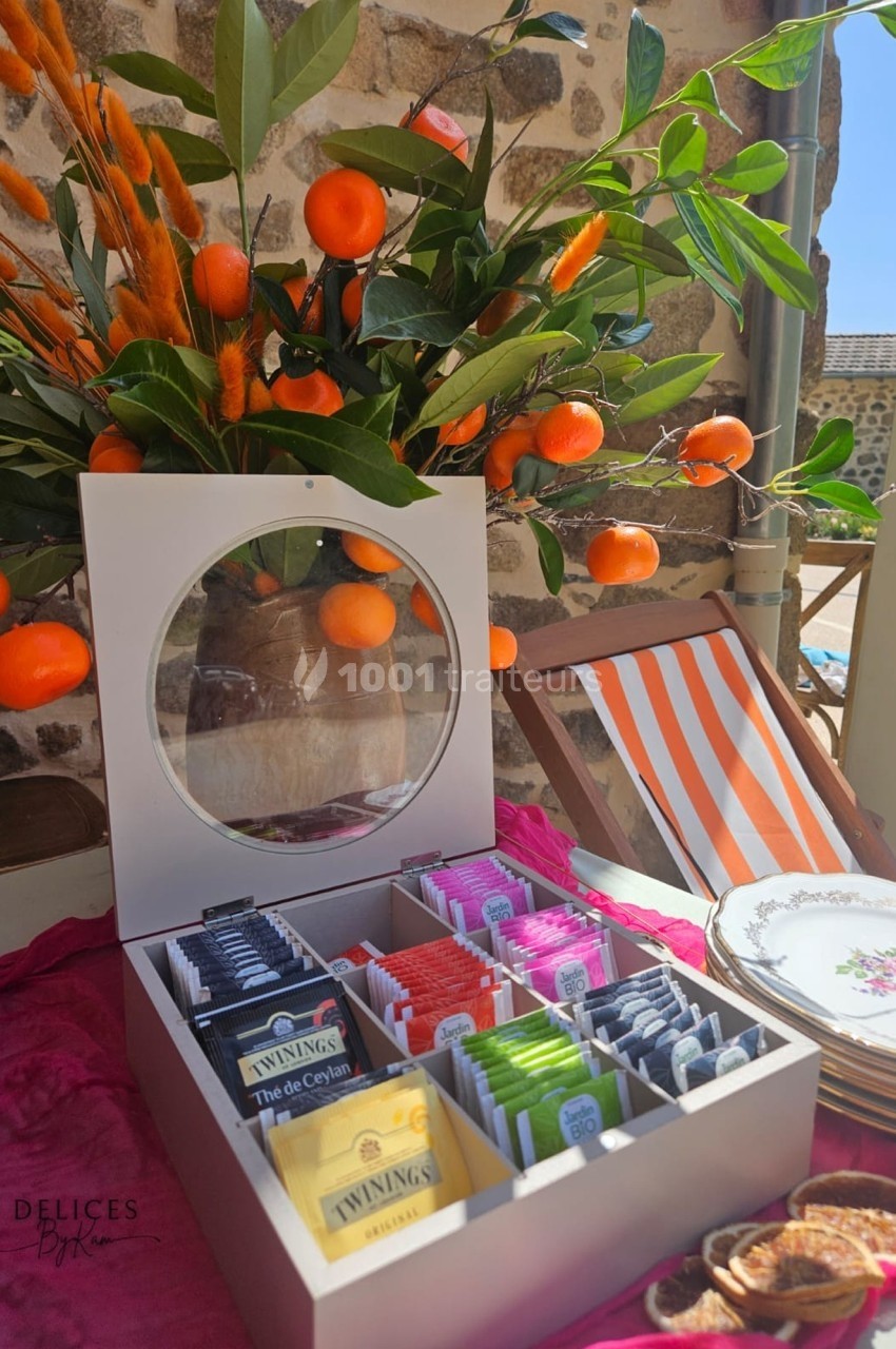 Boîte ouverte contenant des sachets de thé variés, posée sur une table décorée avec des branches d'oranges et de la…