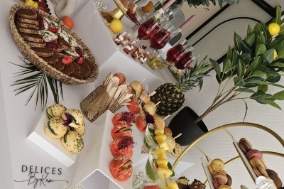 Buffet décoré avec des fleurs, fruits frais, verrines, mini-burgers et desserts, présenté sur une table élégante.