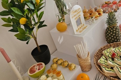 Buffet décoré avec des fleurs, fruits frais, verrines, mini-burgers et desserts, présenté sur une table élégante.