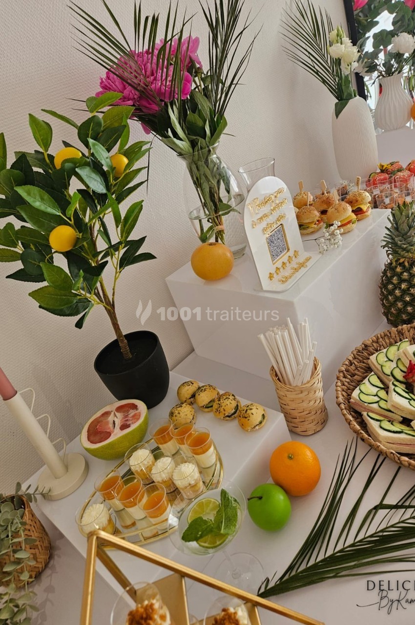 Buffet décoré avec des fleurs, fruits frais, verrines, mini-burgers et desserts, présenté sur une table élégante.