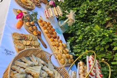 Buffet en extérieur avec divers plats, viennoiseries, fruits et boissons, disposés sur une table blanche décorée de fleurs.