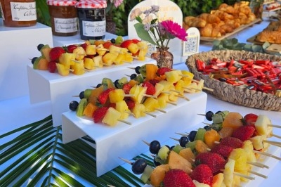 Buffet décoré avec des fleurs, fruits frais, verrines, mini-burgers et desserts, présenté sur une table élégante.
