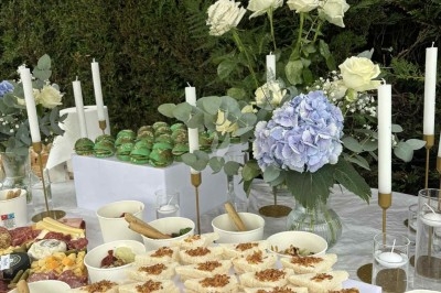 Buffet décoré avec des fleurs, fruits frais, verrines, mini-burgers et desserts, présenté sur une table élégante.