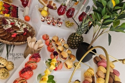 Buffet décoré avec des fleurs, fruits frais, verrines, mini-burgers et desserts, présenté sur une table élégante.