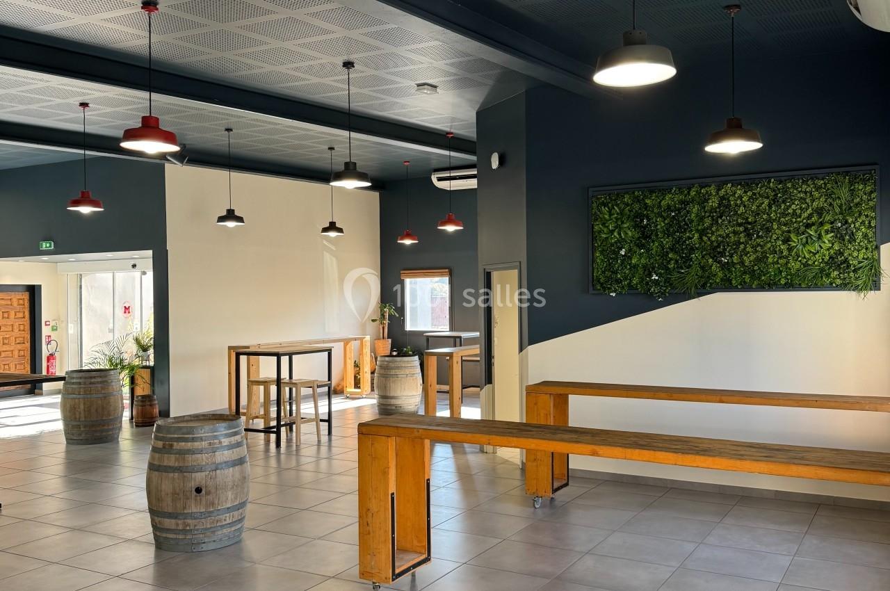 Salle lumineuse avec tables en bois, tonneaux décoratifs, murs bleu foncé et panneau végétal mural.