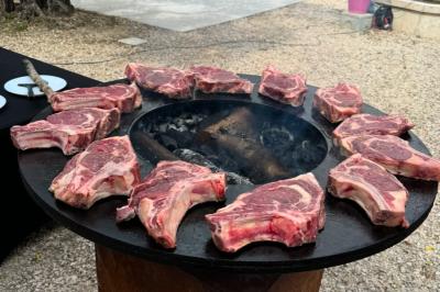 Brochettes variées grillant sur un barbecue circulaire avec un feu central, disposées en cercle.