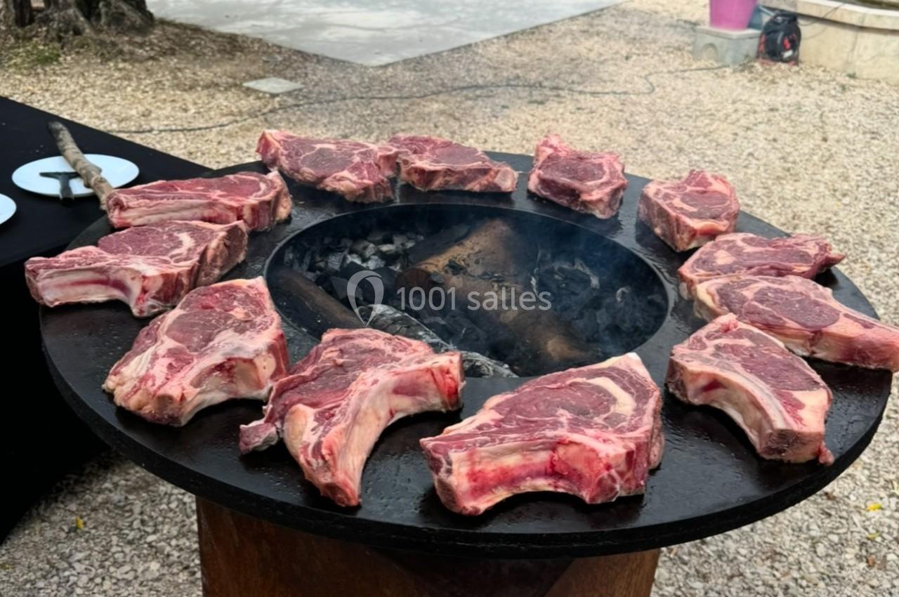 Côtelettes de bœuf crues disposées en cercle sur une plancha ronde chauffée au feu de bois.